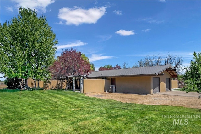 back of house featuring stucco siding, a yard, and metal roof