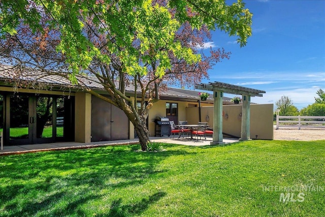 rear view of house with fence, stucco siding, french doors, a patio area, and a yard