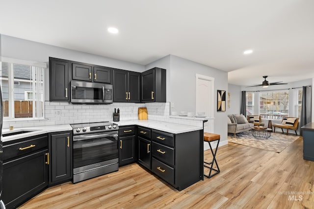 kitchen with kitchen peninsula, tasteful backsplash, stainless steel appliances, ceiling fan, and light hardwood / wood-style floors