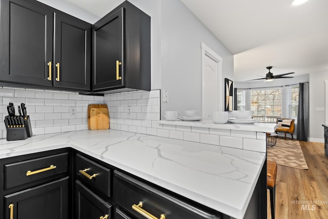 kitchen with backsplash, light hardwood / wood-style flooring, ceiling fan, light stone countertops, and kitchen peninsula