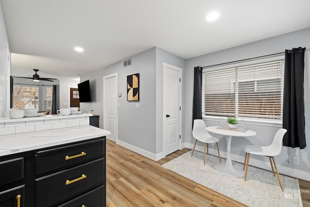 kitchen with light wood-type flooring, light stone counters, and ceiling fan