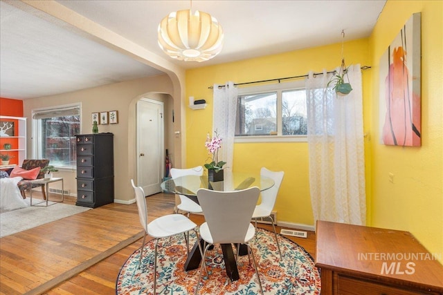 dining area featuring wood finished floors, arched walkways, a wealth of natural light, and baseboards