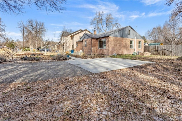 rear view of property featuring brick siding, a chimney, and fence