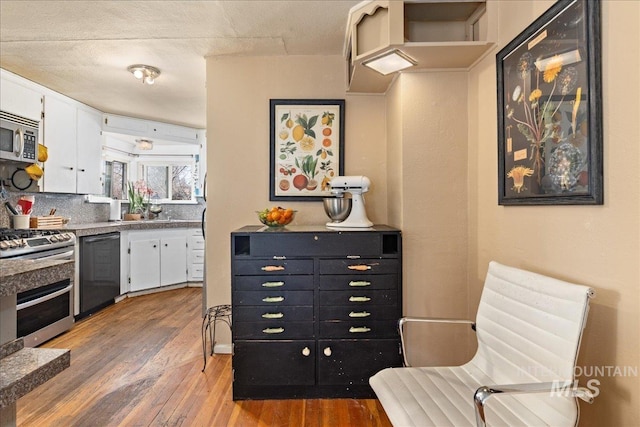 kitchen featuring stainless steel appliances, backsplash, wood finished floors, and white cabinetry