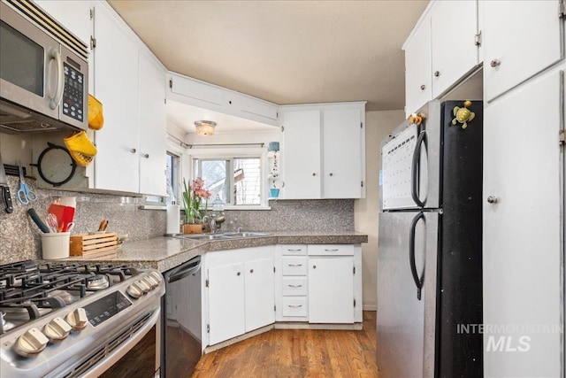 kitchen with tasteful backsplash, appliances with stainless steel finishes, wood finished floors, white cabinets, and a sink