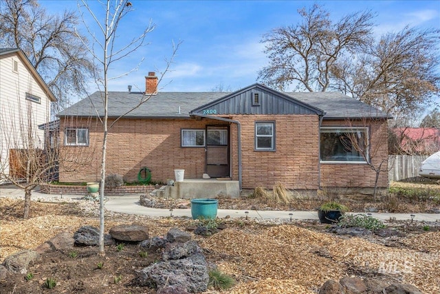 back of house featuring brick siding, a chimney, and fence