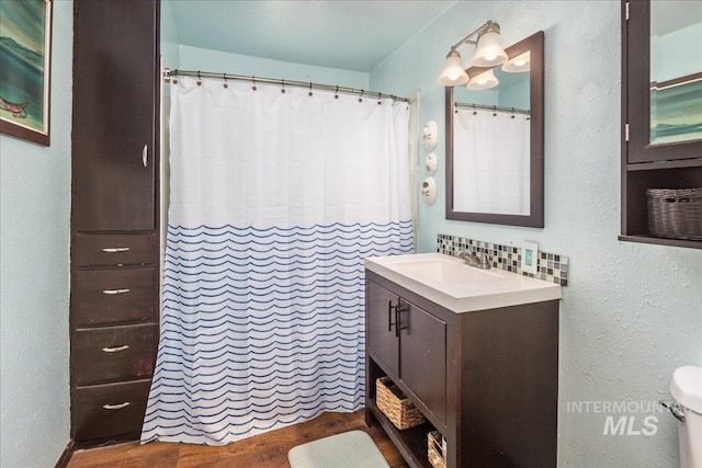 bathroom featuring vanity, wood finished floors, toilet, a textured wall, and backsplash