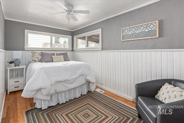 bedroom with wainscoting, visible vents, ornamental molding, and wood-type flooring