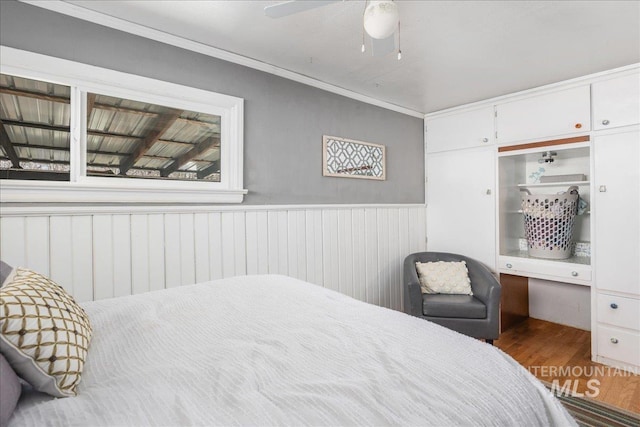 bedroom featuring a wainscoted wall, crown molding, a ceiling fan, and wood finished floors