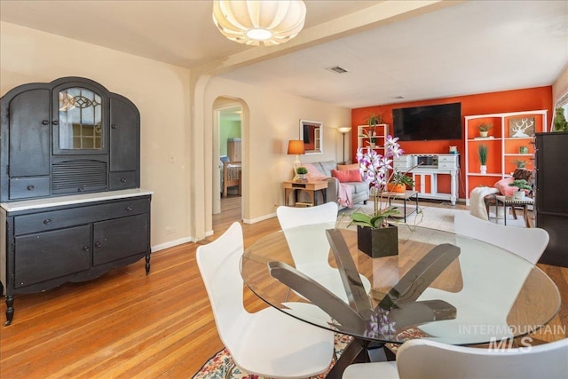 dining space with baseboards, visible vents, arched walkways, and light wood-type flooring