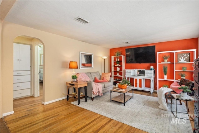 living room with arched walkways, visible vents, baseboards, and wood finished floors