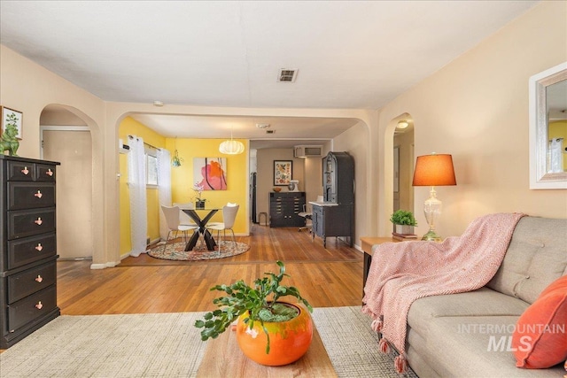 living area featuring arched walkways, visible vents, and wood finished floors