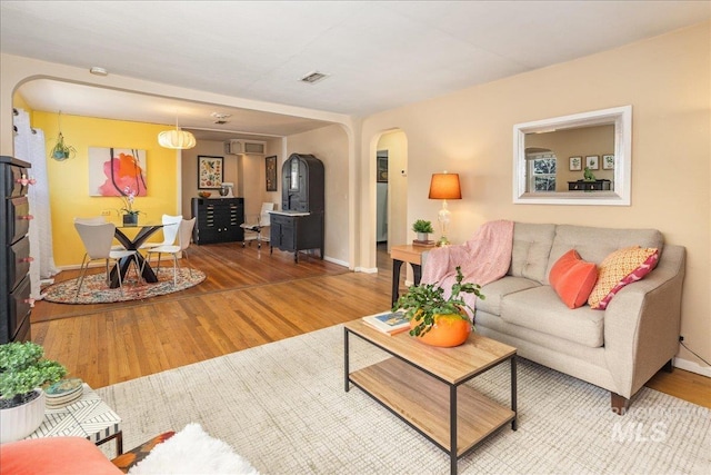 living room featuring visible vents, baseboards, a wall unit AC, wood finished floors, and arched walkways