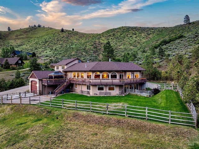 back of property at dusk featuring a deck with mountain view, fence private yard, a yard, and stairway