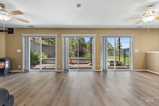 unfurnished living room featuring a wood stove, baseboards, visible vents, and wood finished floors