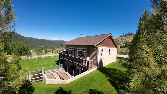 rear view of house featuring roof with shingles, a lawn, a deck with mountain view, and fence