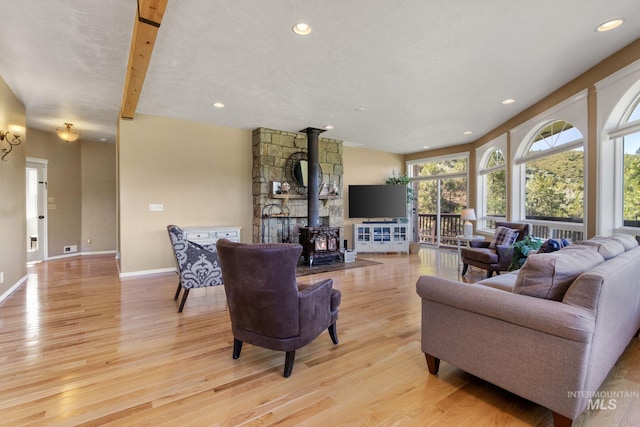 living room with a textured ceiling, light wood-style flooring, recessed lighting, baseboards, and a wood stove