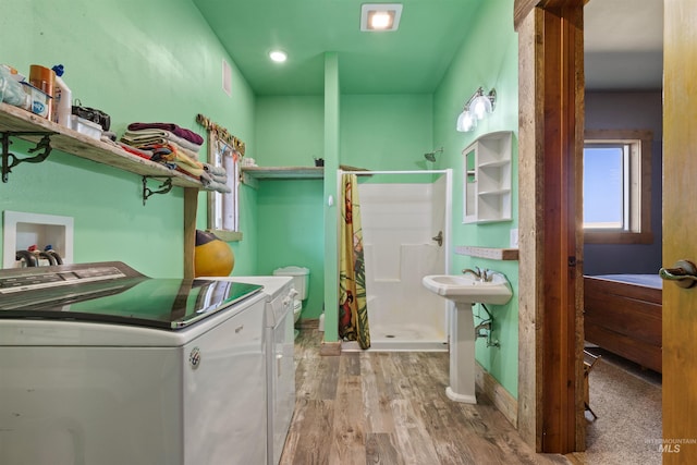 laundry area featuring laundry area, wood finished floors, a sink, washing machine and dryer, and baseboards
