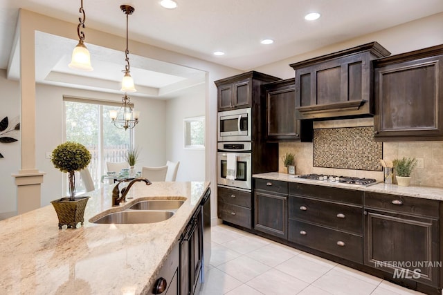 kitchen with a sink, a tray ceiling, decorative light fixtures, tasteful backsplash, and appliances with stainless steel finishes