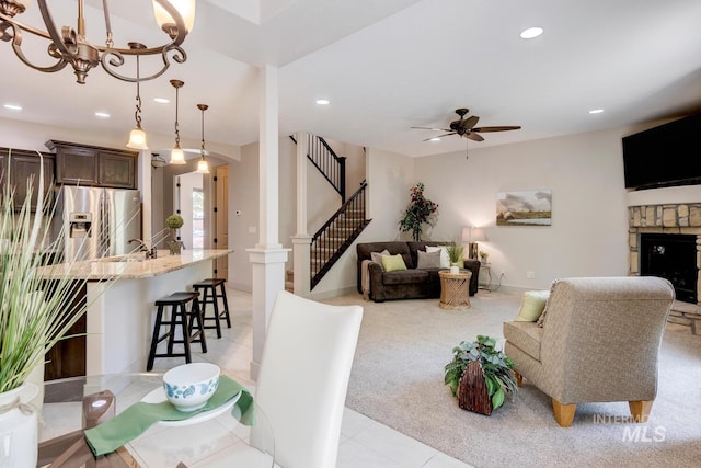 living area featuring light colored carpet, decorative columns, recessed lighting, a fireplace, and ceiling fan with notable chandelier