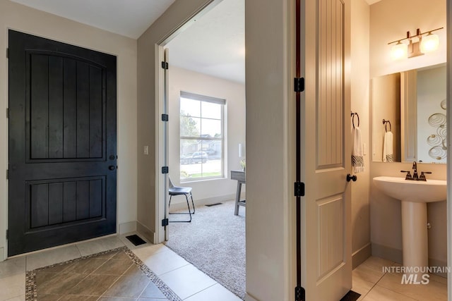 entrance foyer featuring light tile patterned floors, baseboards, and light colored carpet