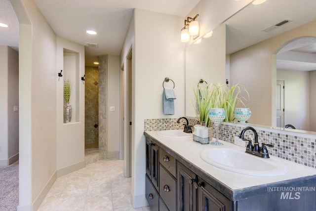 full bathroom featuring tiled shower, visible vents, backsplash, and a sink