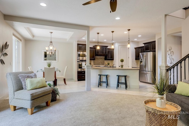 living room with stairs, light carpet, light tile patterned floors, a raised ceiling, and a ceiling fan