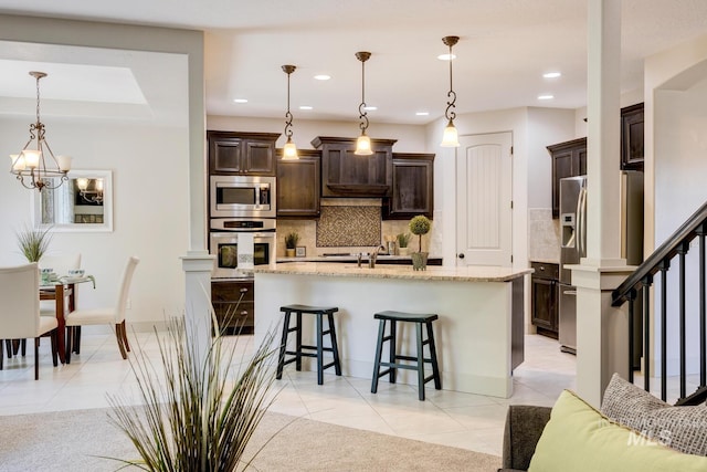 kitchen featuring dark brown cabinets, appliances with stainless steel finishes, a breakfast bar area, and light tile patterned flooring