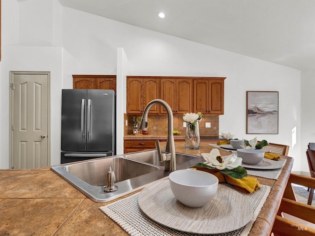 kitchen featuring freestanding refrigerator, a sink, brown cabinets, high vaulted ceiling, and recessed lighting