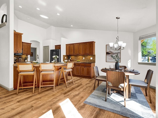 dining space with a chandelier, light wood-type flooring, recessed lighting, arched walkways, and high vaulted ceiling
