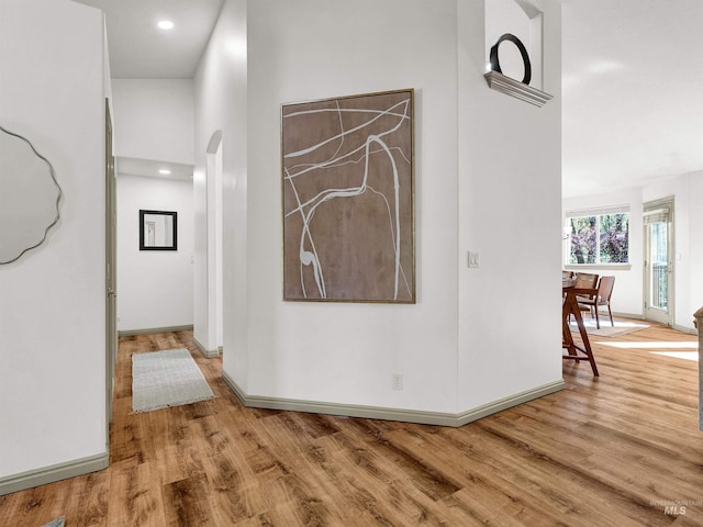 hallway featuring wood finished floors, baseboards, arched walkways, and recessed lighting