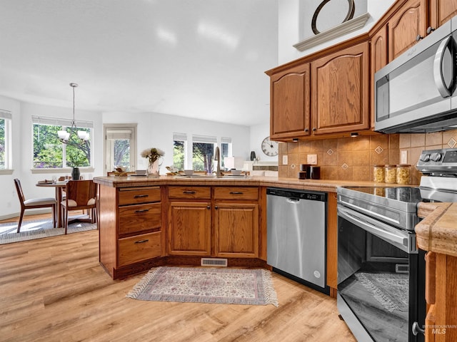 kitchen featuring appliances with stainless steel finishes, a peninsula, light wood finished floors, and brown cabinets