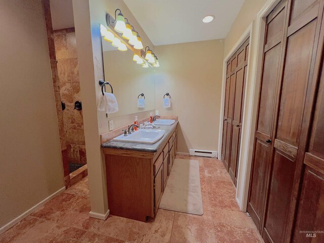 full bath featuring tiled shower, double vanity, a baseboard heating unit, and a sink