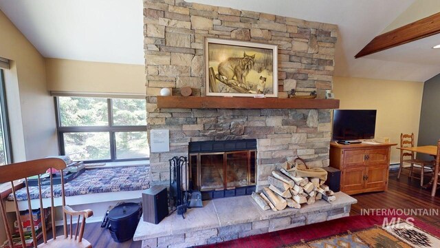 living room featuring a stone fireplace, wood finished floors, and lofted ceiling