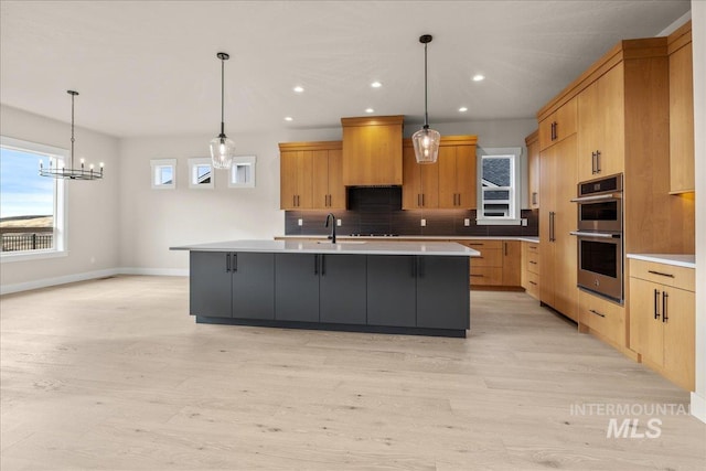 kitchen featuring a spacious island, pendant lighting, stainless steel double oven, backsplash, and light wood-type flooring