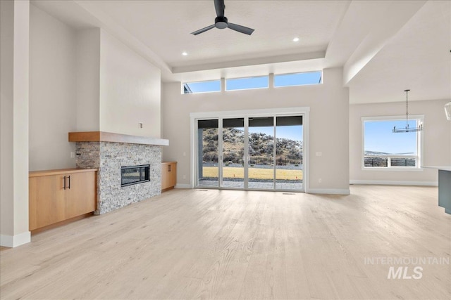 unfurnished living room featuring ceiling fan, light hardwood / wood-style floors, and a stone fireplace