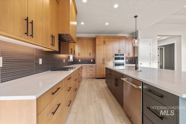 kitchen featuring pendant lighting, a large island with sink, stainless steel appliances, decorative backsplash, and light hardwood / wood-style flooring