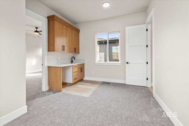 kitchen with ceiling fan, light brown cabinetry, and light colored carpet