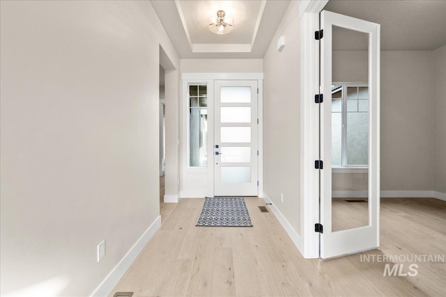 entryway with light hardwood / wood-style floors and a tray ceiling