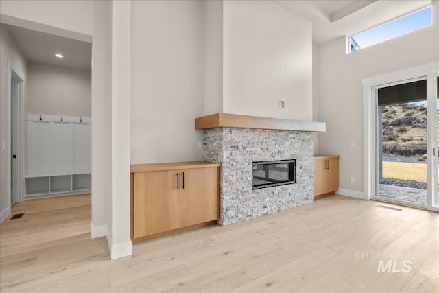 unfurnished living room with a fireplace, a towering ceiling, and light hardwood / wood-style floors