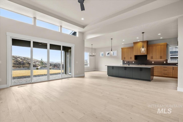 kitchen featuring ceiling fan with notable chandelier, a large island with sink, backsplash, hanging light fixtures, and light wood-type flooring