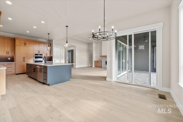 kitchen with an inviting chandelier, a healthy amount of sunlight, pendant lighting, and an island with sink