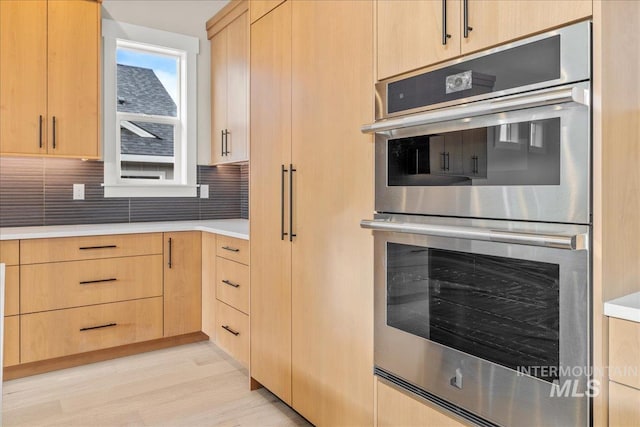 kitchen with tasteful backsplash, stainless steel double oven, light brown cabinetry, and light hardwood / wood-style flooring