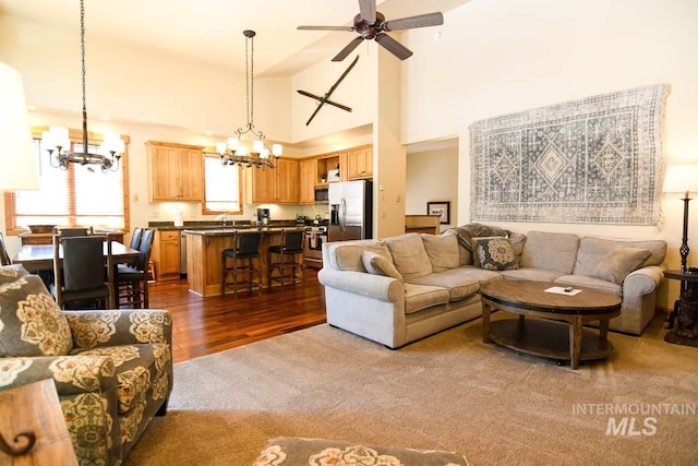 living room with dark colored carpet, ceiling fan with notable chandelier, dark wood finished floors, and a towering ceiling