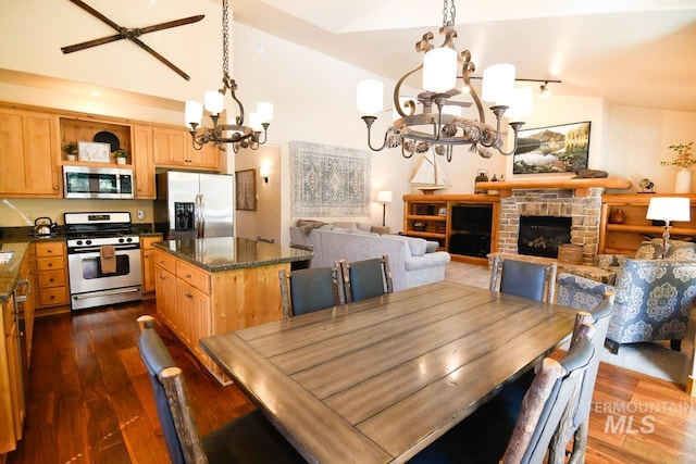 dining space featuring dark wood finished floors, lofted ceiling, a notable chandelier, and a fireplace