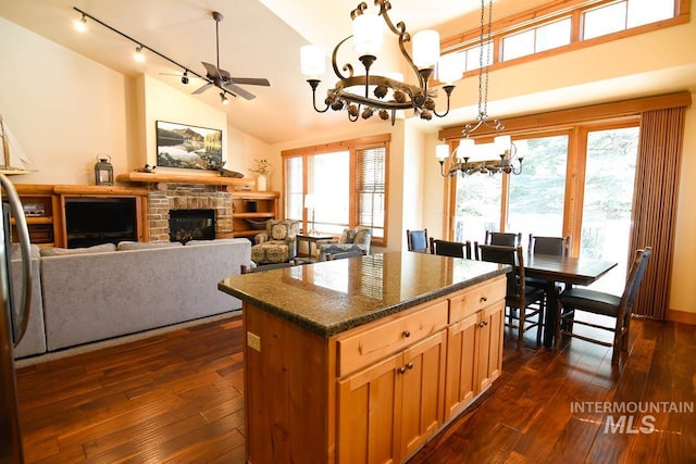 kitchen with a kitchen island, dark wood finished floors, a stone fireplace, and dark stone countertops