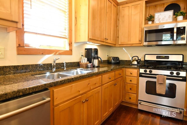 kitchen with a sink, dark wood-style flooring, appliances with stainless steel finishes, and dark stone counters