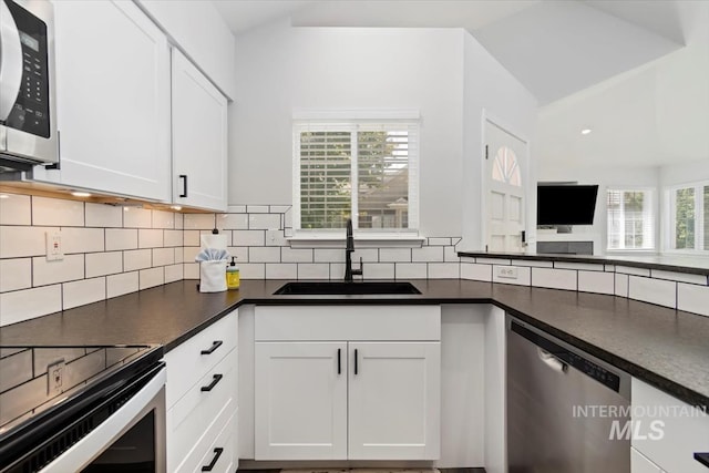 kitchen with a sink, white cabinets, appliances with stainless steel finishes, dark countertops, and tasteful backsplash