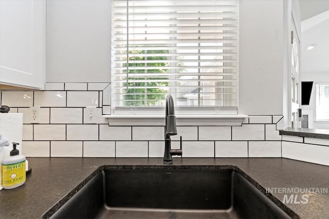 details with a sink, tasteful backsplash, white cabinets, and dark stone countertops