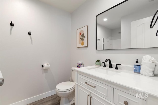 bathroom with vanity, wood finished floors, baseboards, a shower, and toilet